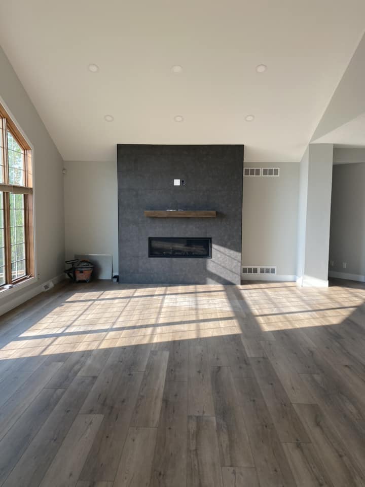 Finished great room with floor-to-ceiling dark tile fireplace surround, raw wood mantel, linear gas fireplace, and vaulted ceiling